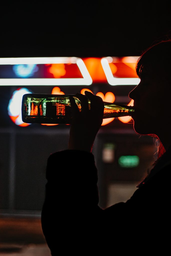 neon lights in background with person drinking from a bottle in foreground