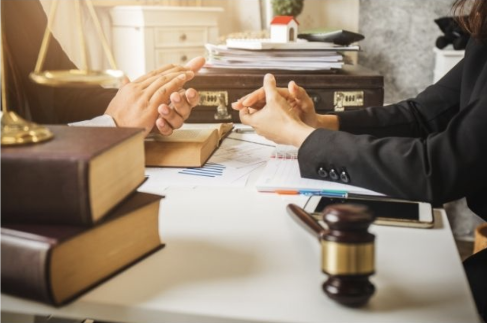 closeup of two people in conversation with law books and a gavel in foreground