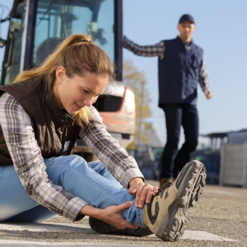 woman holding her ankle while guy in background steps down from forklift