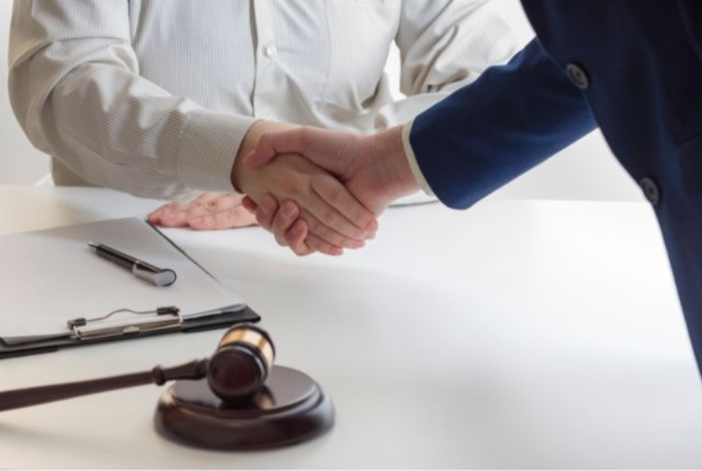 a client shakes hands with his personal injury lawyer across a desk with a gavel and a notepad on top.