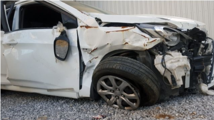 front of white car damaged in a severe accident sitting on gravel, some rust