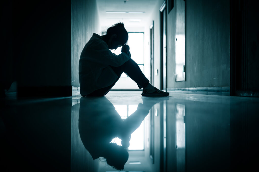 girl sitting against a wall in a hallway with her head down struggling with depression following an accident