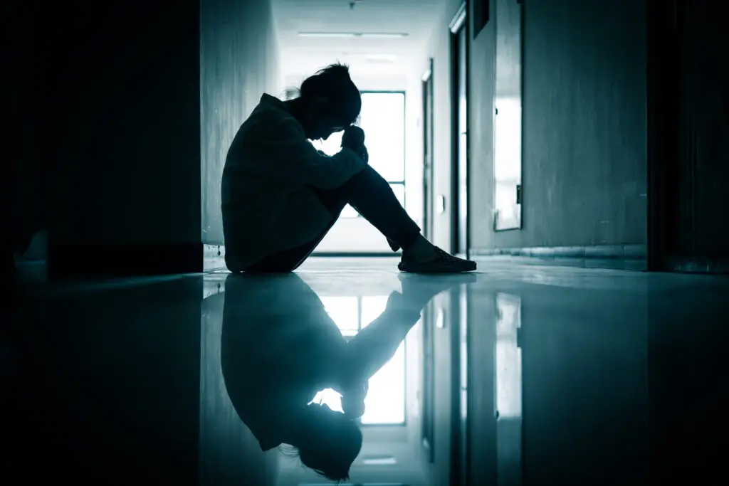 woman sitting in a hallway with her hands on her head, mental health theme