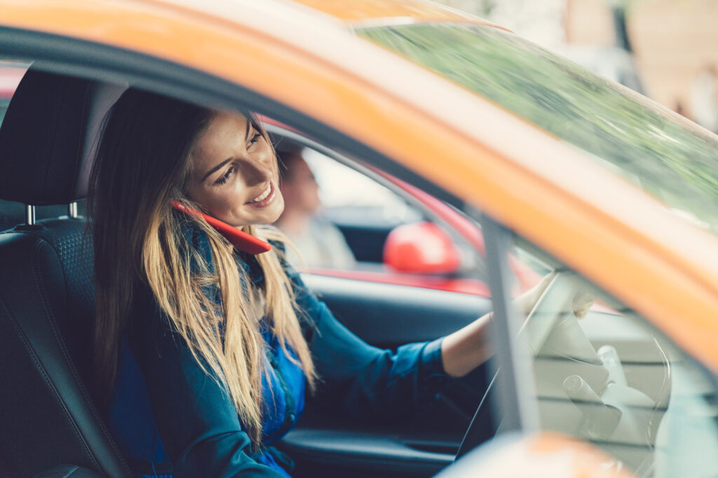 Smiling woman talking on phone while driving a car with insurance