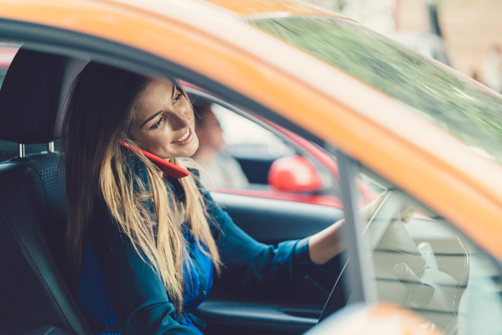 Smiling woman talking on phone while driving a car.