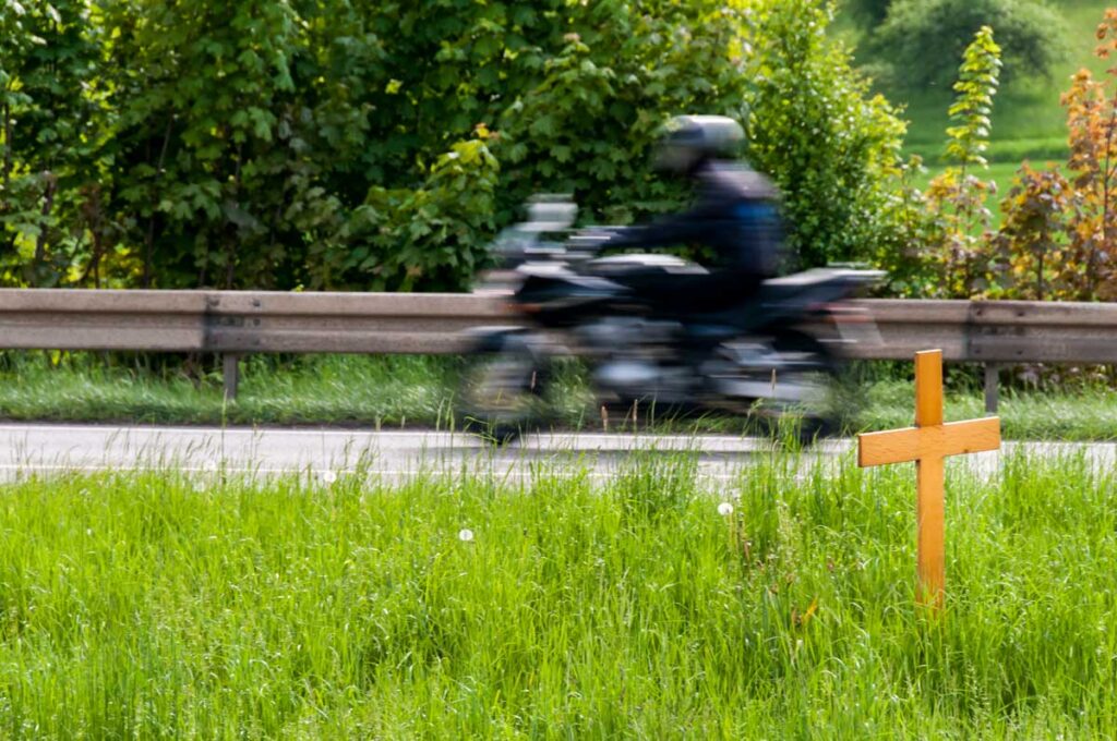 motorcyclist on the road passing a cross in the grass marking the passing away of someone on that road