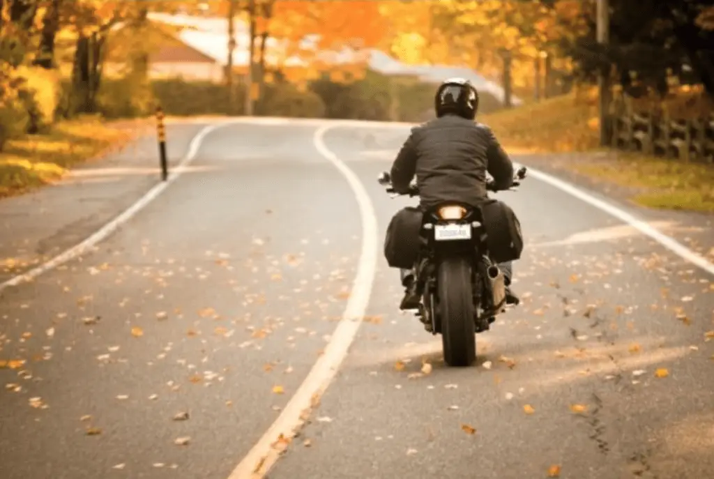A motorcyclist drives down a leaf-covered, curving road