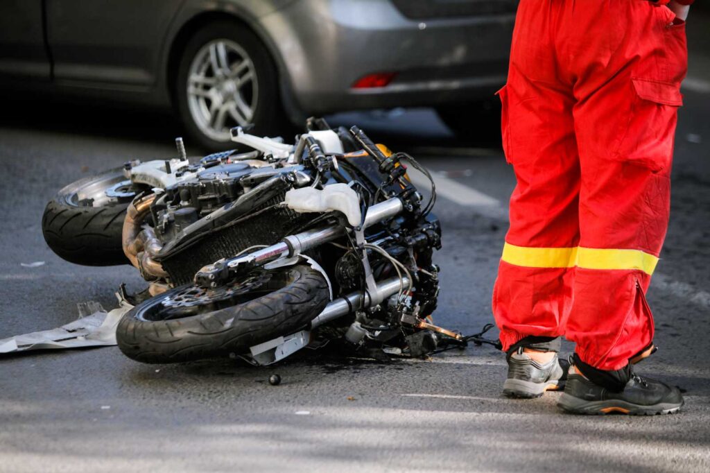 a person in bright orange pants stands over a damaged motorcycle after an accident.