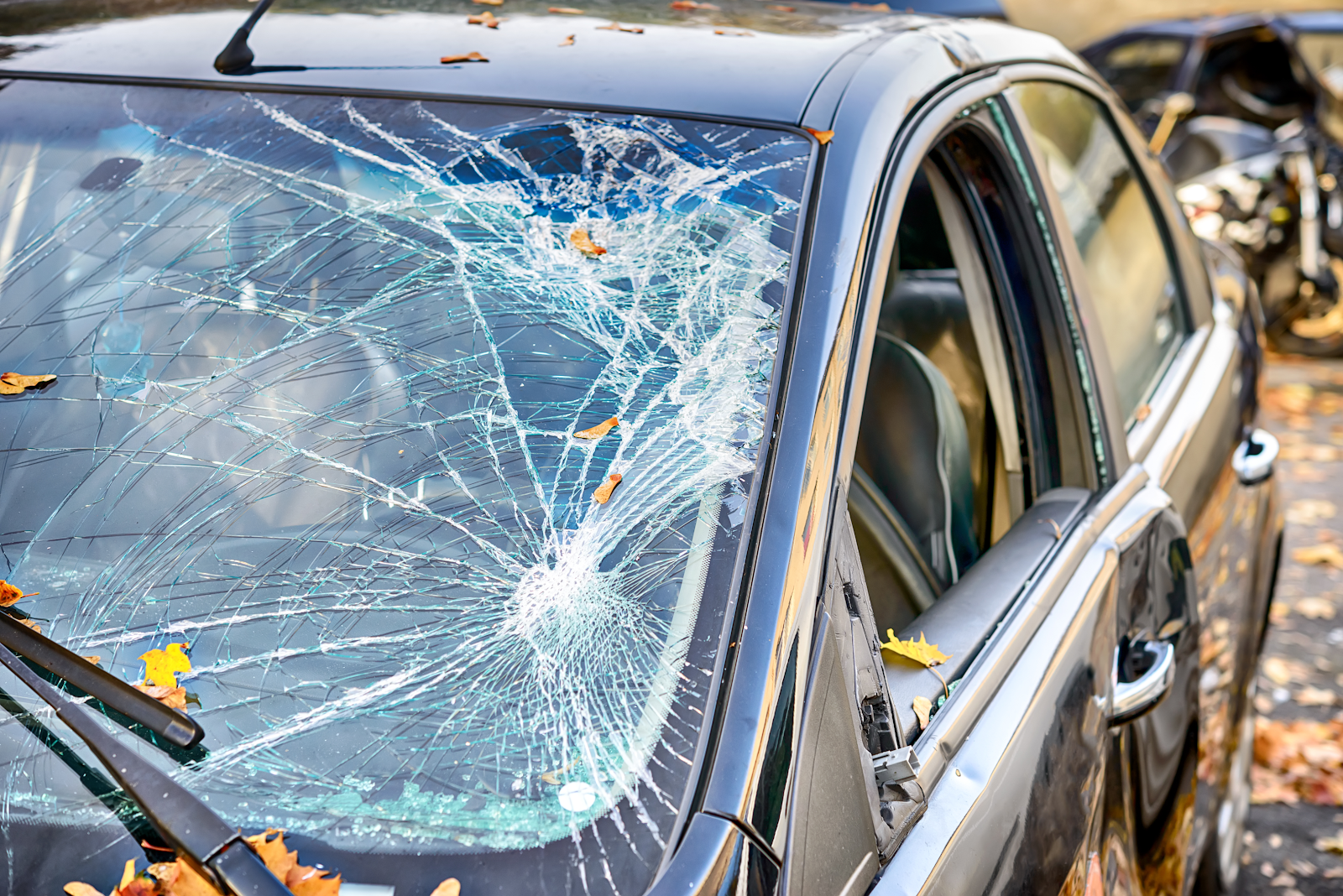 A close-up of a damaged vehicle with a heavily cracked windshield and dents in the driver side door.