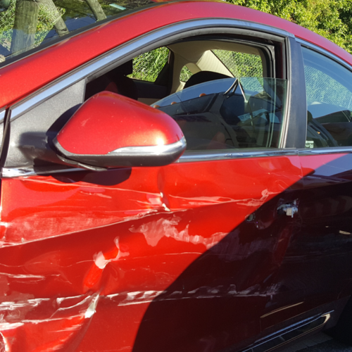 A close-up picture of a red car that has damage to its drivers-side door, the result of a car accident in Clearwater