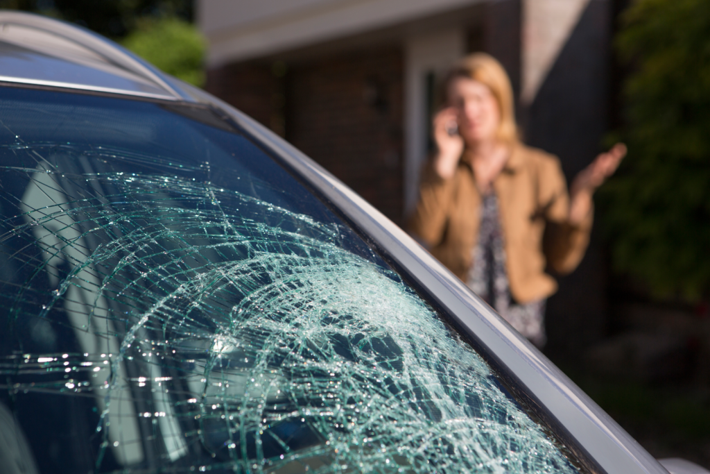 woman on the phone looking at her damaged car window discussing homeowner's insurance policy exclusions