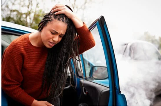 A woman exits her car after an accident, holding her head in pain.