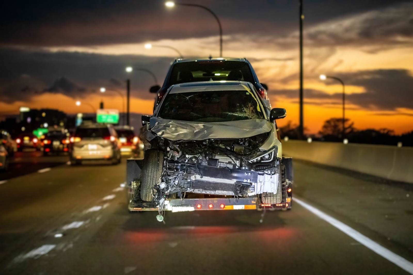 A damaged vehicle is being towed to a junkyard on a flatbed tow truck after being totaled in an accident.