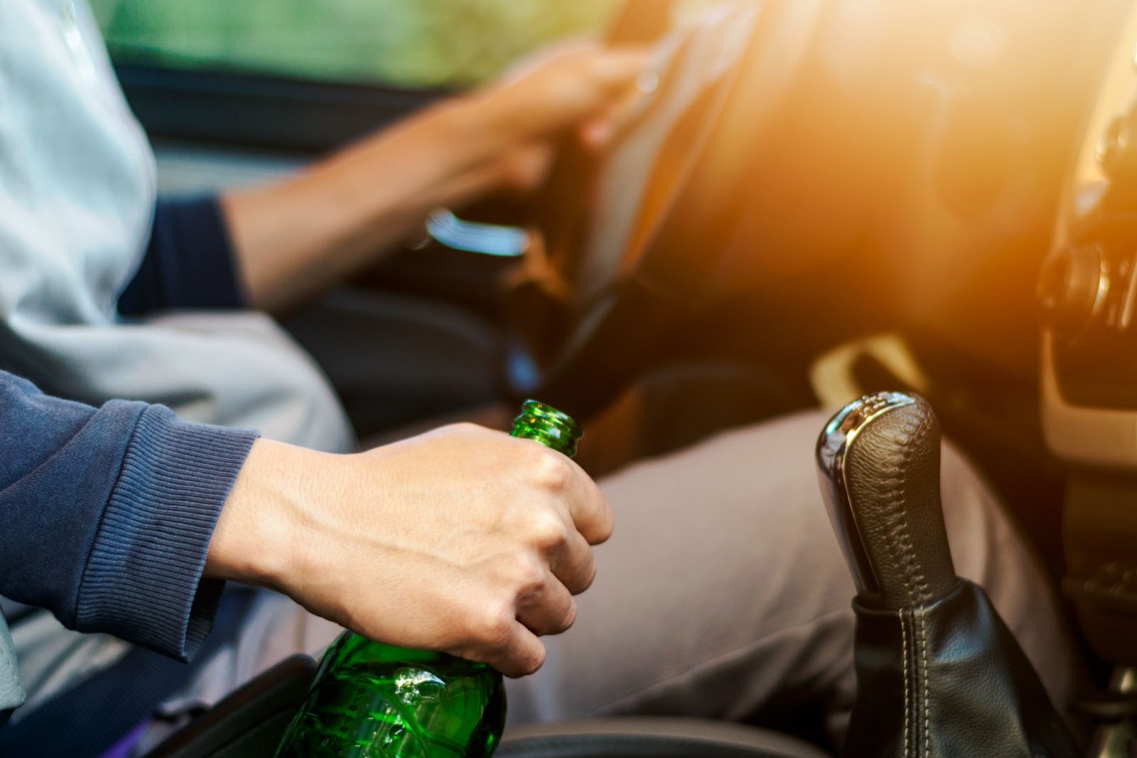 a driver of an automobile has a bottle of beer in their cupholder.