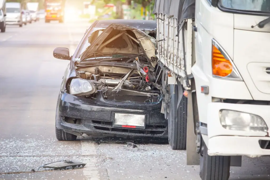 A heavily damaged black sedan after an accident with a large commercial truck. 