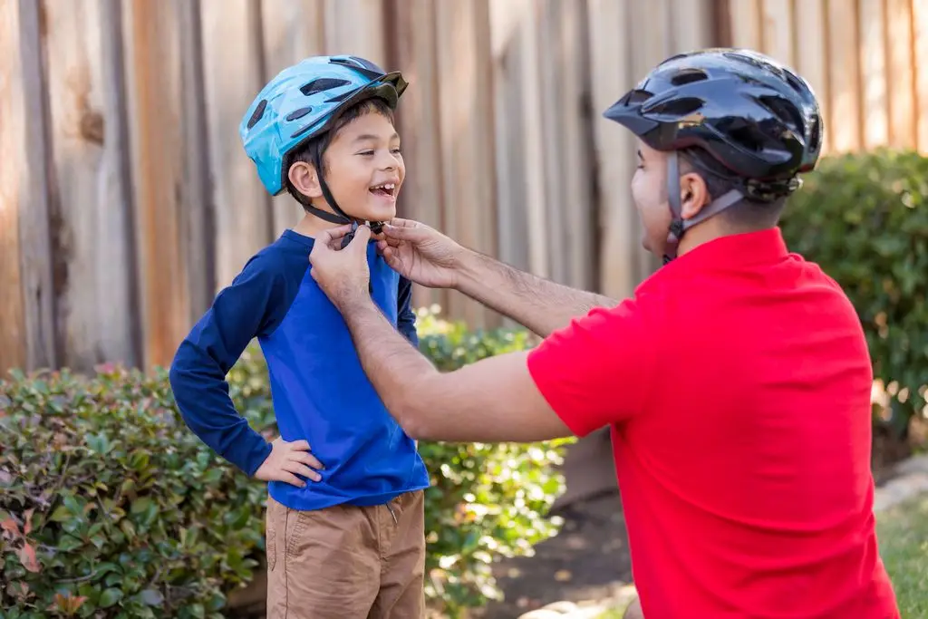 A father fastens the chinstrap on his sons bicycle helmet before going out for a ride