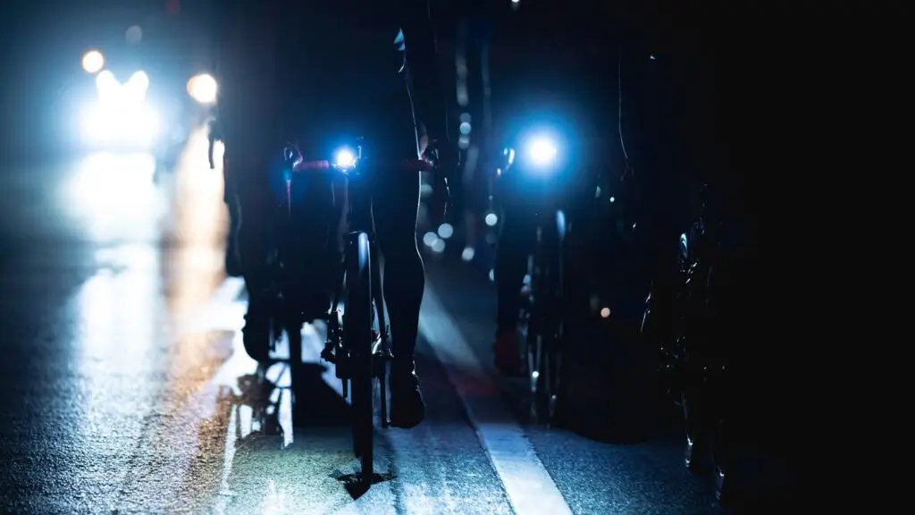 Cyclists riding at night with headlights on the front of their bikes.