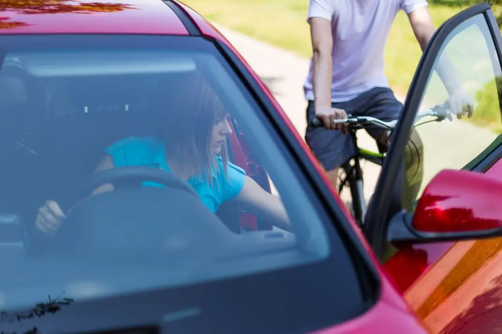 a woman opens her car door into the path of an oncoming bicyclist, causing a "dooring" accident.