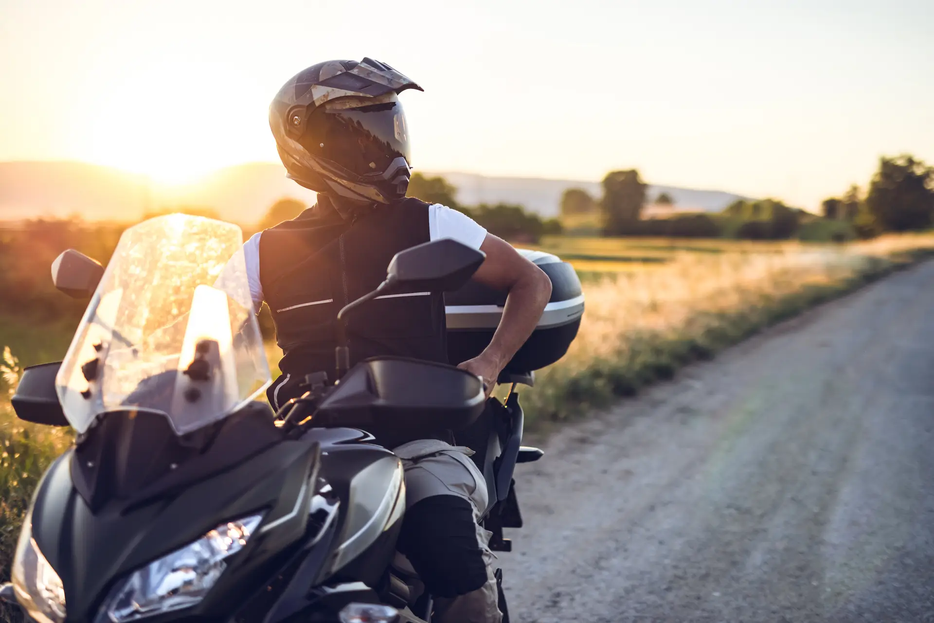 A motorcyclist stops to admire the sunset on a desolate road while on a road trip.