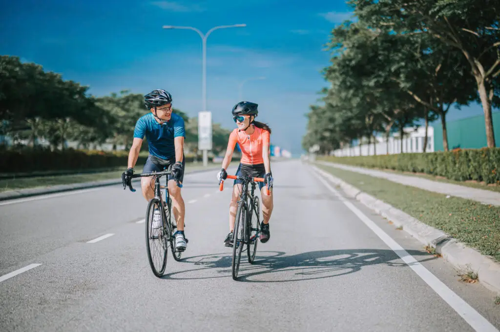 A man and a woman ride their bicycles in the street.