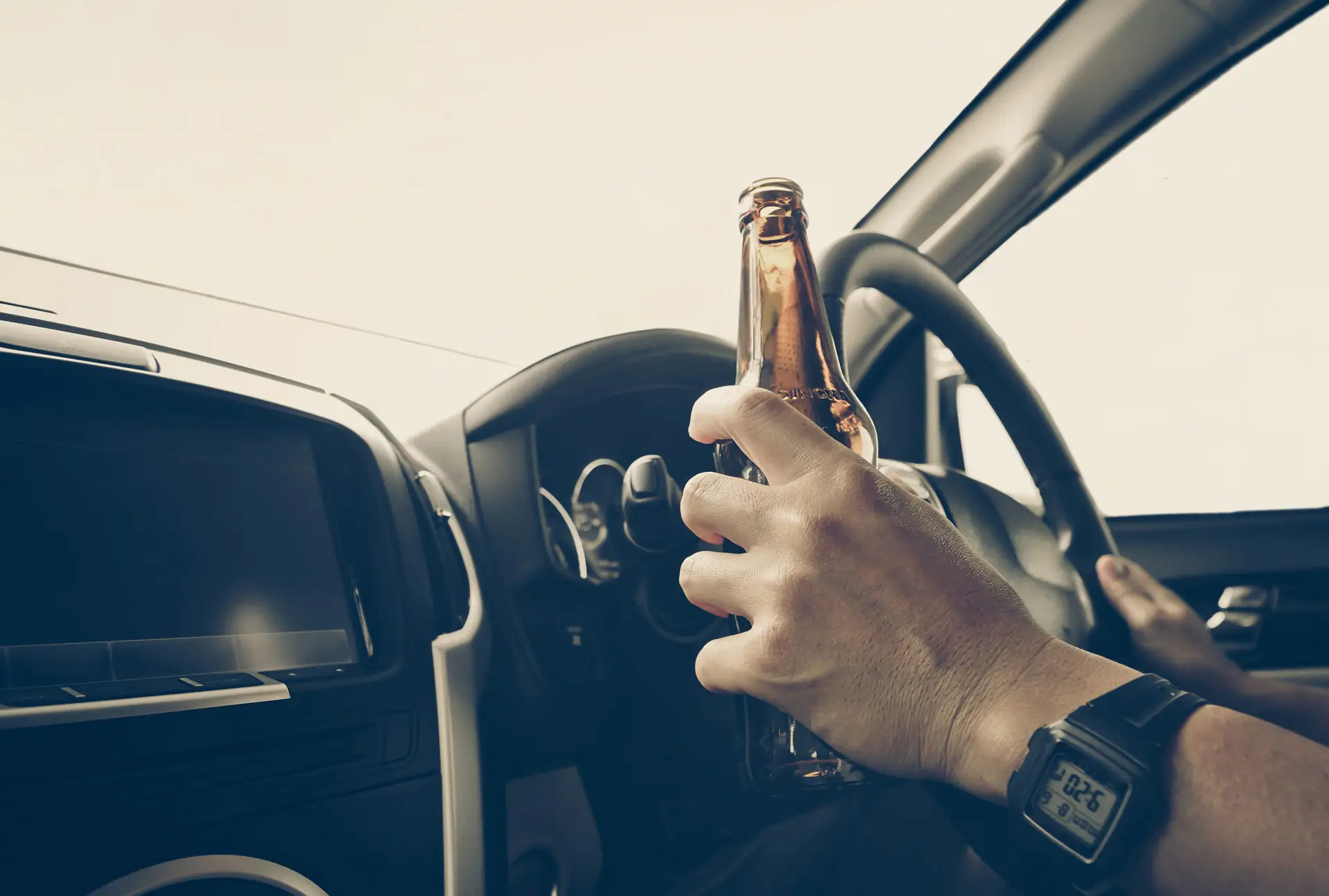 Close up of a steering wheel with the drunk driver having one hand on the wheel, and the other hand holding a beer.