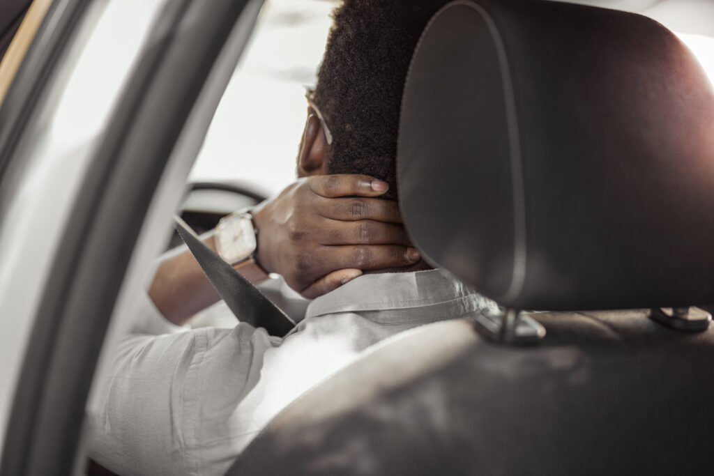 A man holds his neck after a car accident. Wearing a seat belt helped prevent further injuries.