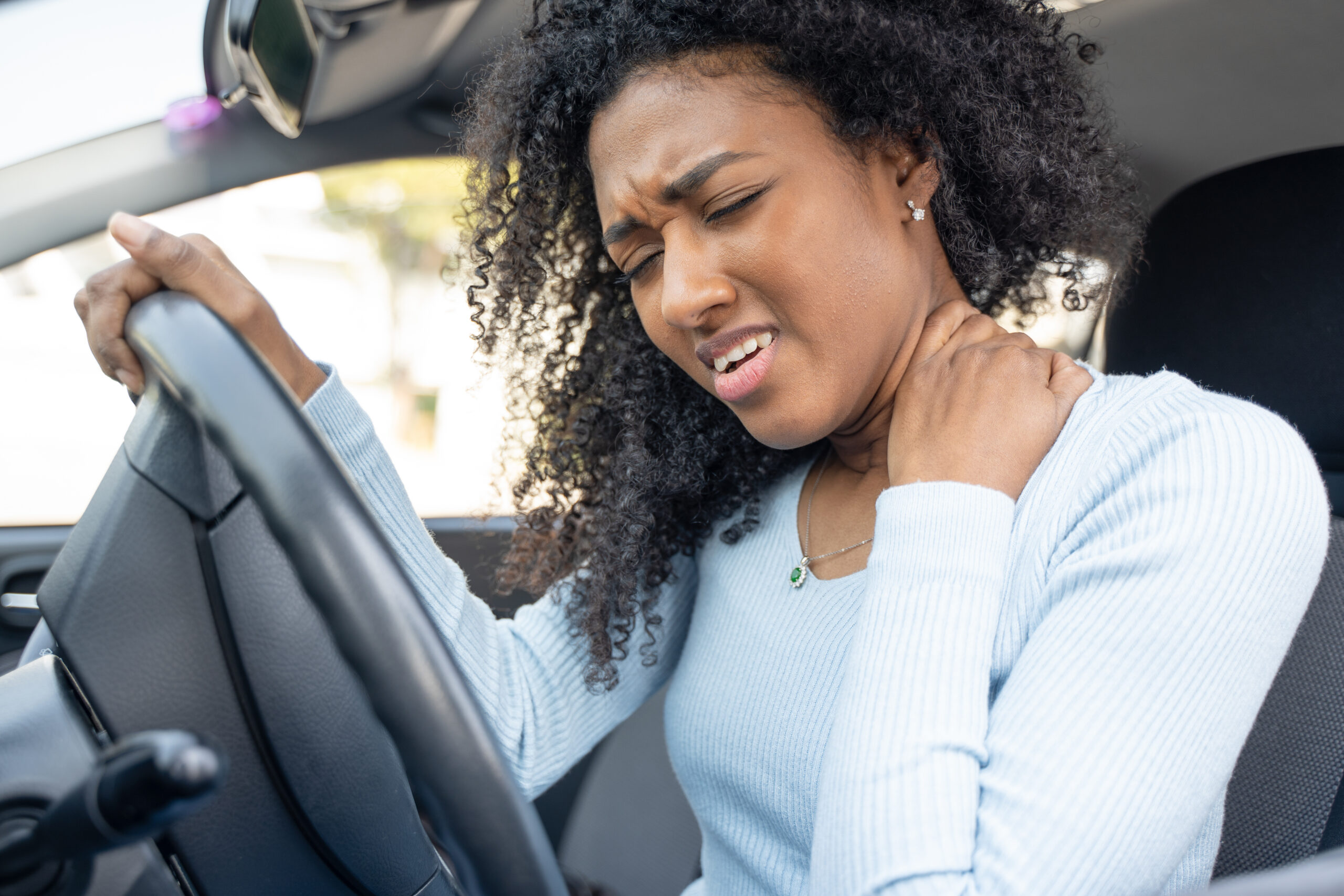 A woman winces in pain and grabs her neck, showing signs of whiplash, after a car accident