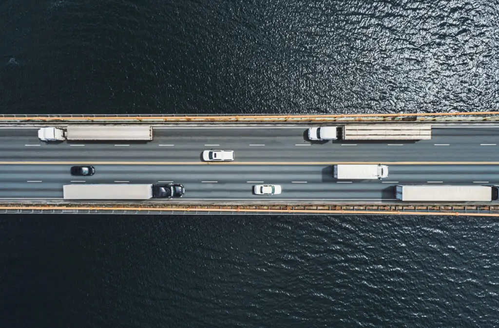 An aerial view of a bridge going over water, with heavy semi-truck and passenger vehicle traffic.