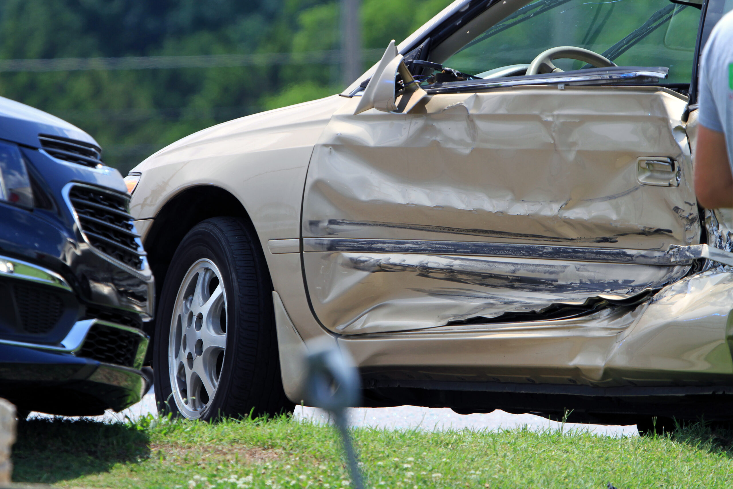 A gold-colored car with extensive damage to the driver's side door after a high-speed accident.