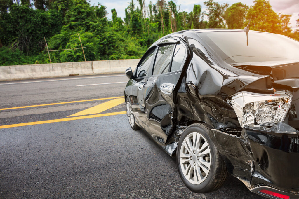 A black sedan with heavy damage to the body sits on the side of the road after a car accident in Brooksville, Florida