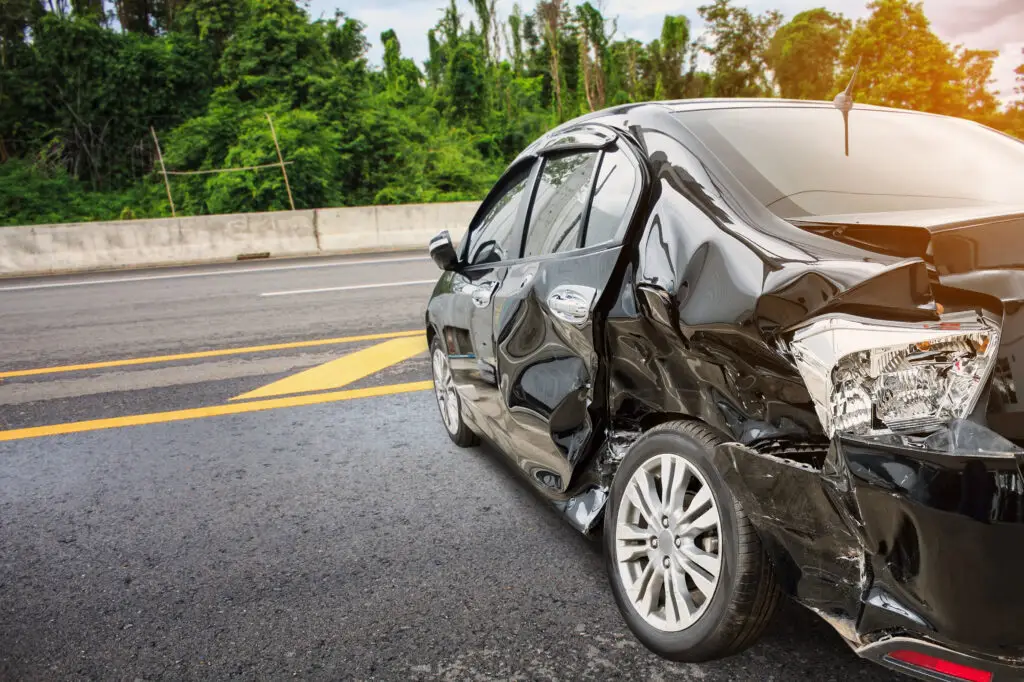 A black sedan with heavy damage to the body sits on the side of the road after a car accident in Brooksville, Florida