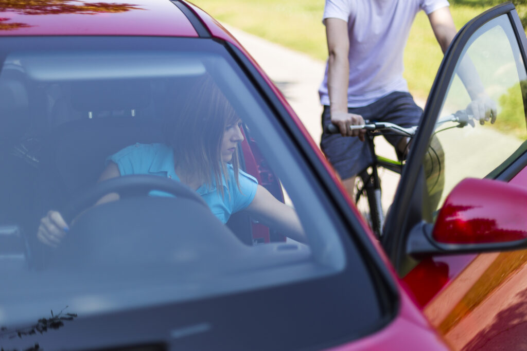 A woman is opening her car door into the path of an oncoming cyclist, leading to a dooring accident.