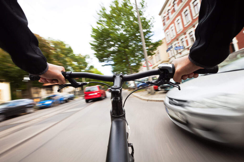A first-person view of a cyclist riding down the street with a car pulling out in front of them at an intersection.