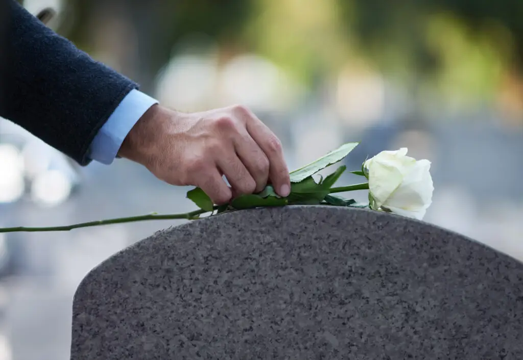 A man places a white rose on top of a gravestone after a funeral.