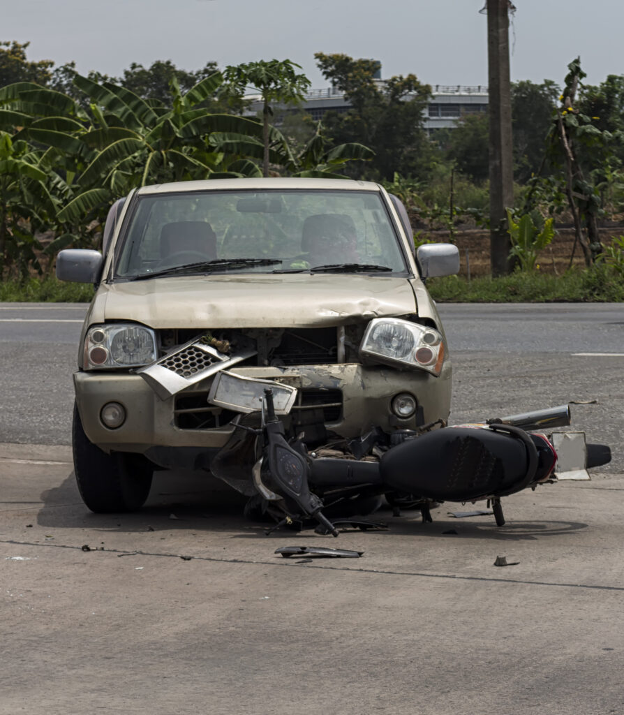 an accident scene involving a brown car and a motorcycle. Both vehicles sustained heavy damage.