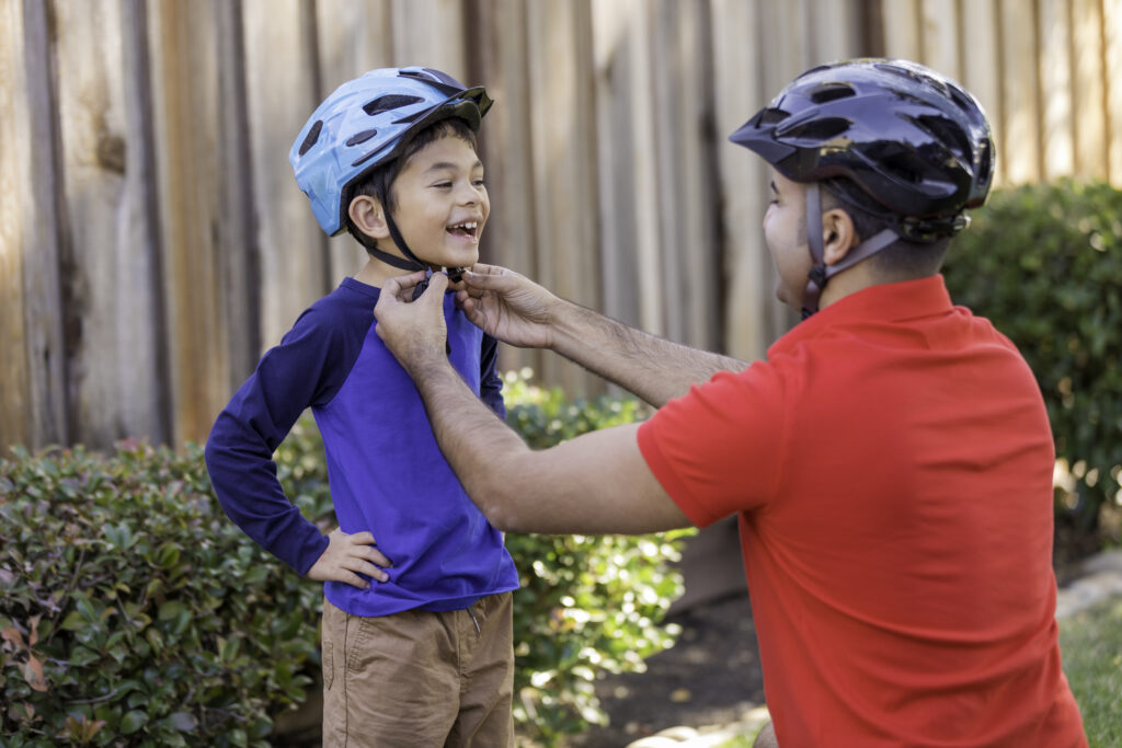 A father straps a bicycle helmet on his son before they go for a bicycle ride.