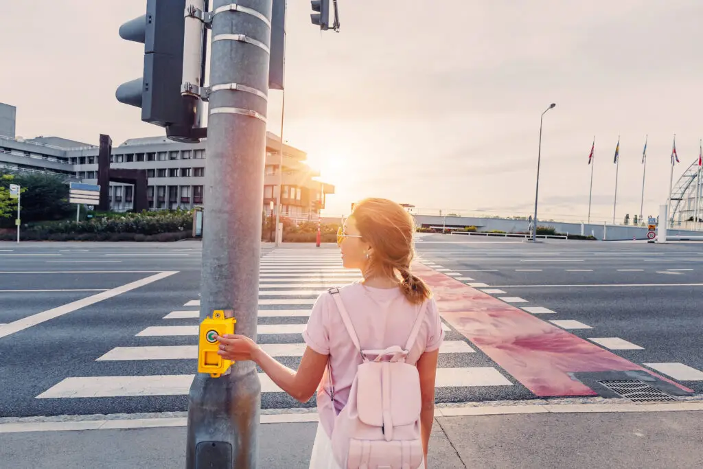 A young gurl presses the walk button at a busy intersection to change the signal to "walk".