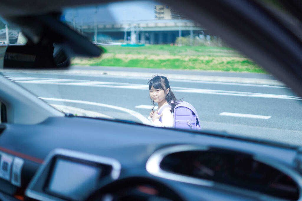 A car approaches a young girl crossing a street at a pedestrian crosswalk.